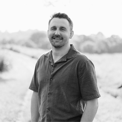 Smiling man in a short-sleeve shirt standing outdoors in a field in black and white.