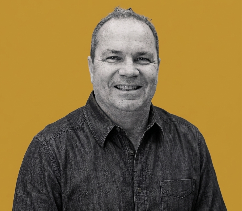 Smiling man in a dark denim shirt, portrait against an orange background.